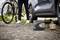 Une personne se tient à côté d'une voiture, tandis qu'un pneu est gonflé à l'aide d'un compresseur portable. Un vélo est appuyé à proximité.