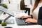 Une personne travaille à un bureau avec un support pour ordinateur portable et un clavier ; à l'arrière-plan, une autre personne est assise à un poste de travail similaire.