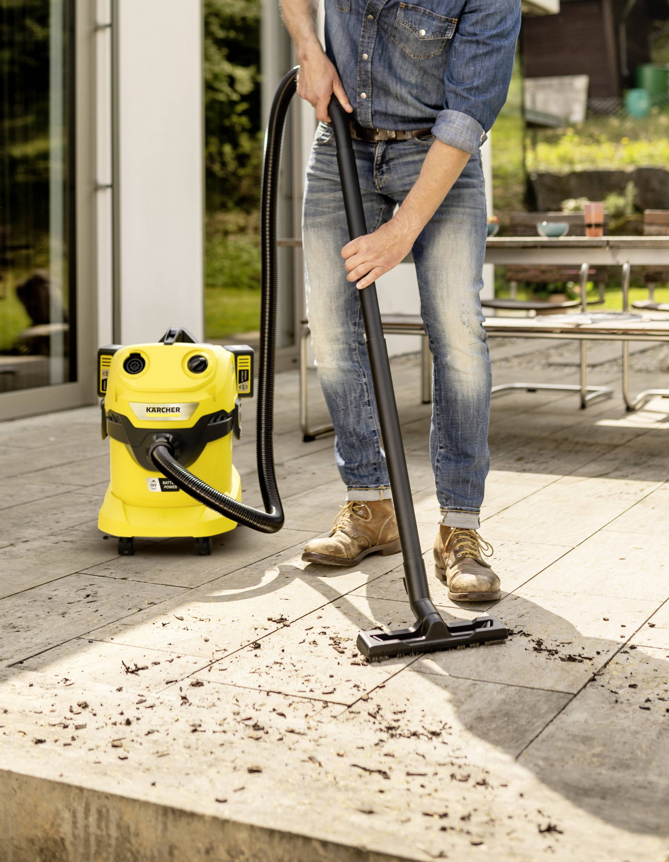 Une personne utilise un aspirateur industriel jaune sur une terrasse en bois pour enlever les saletés et les feuilles.