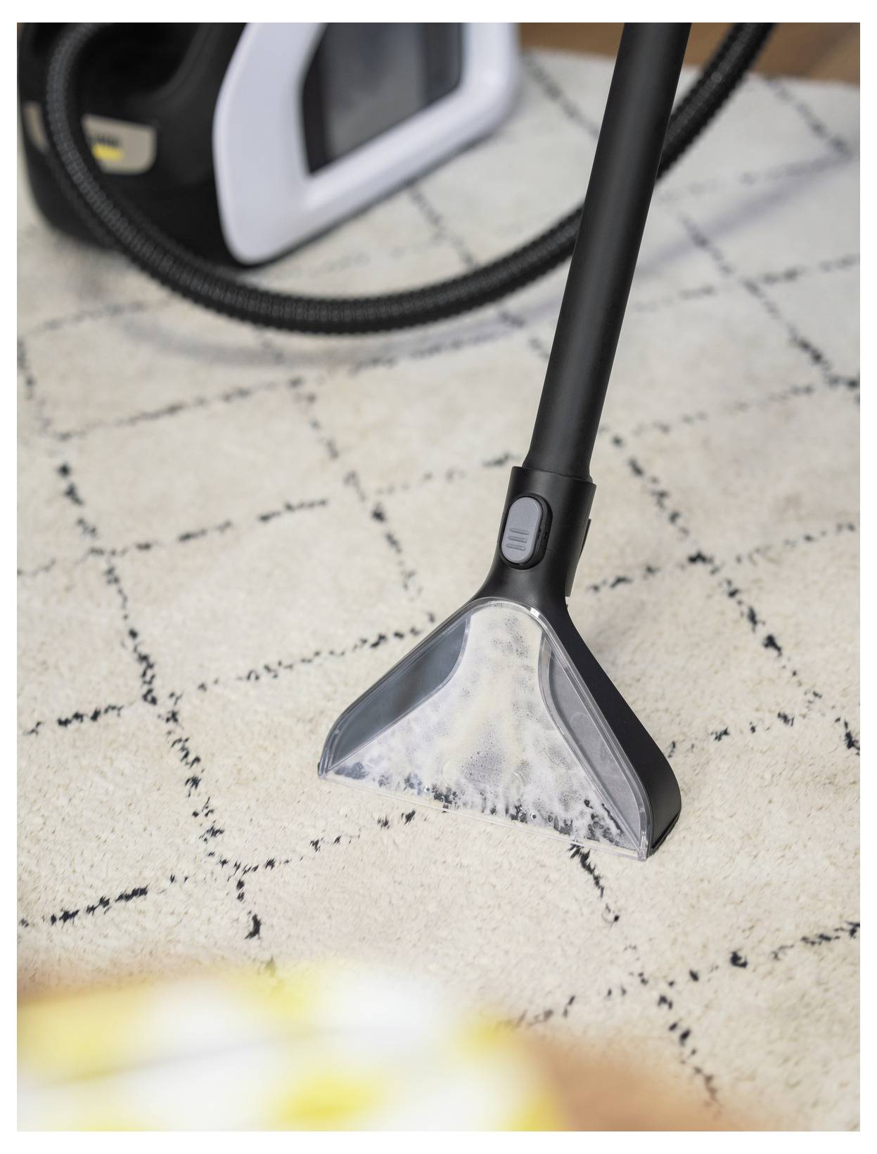 Une tête d'aspirateur sur un tapis de couleur claire. L'aspirateur semble en cours d'utilisation, avec la tête d'aspiration nettoyant visiblement la surface du tapis.