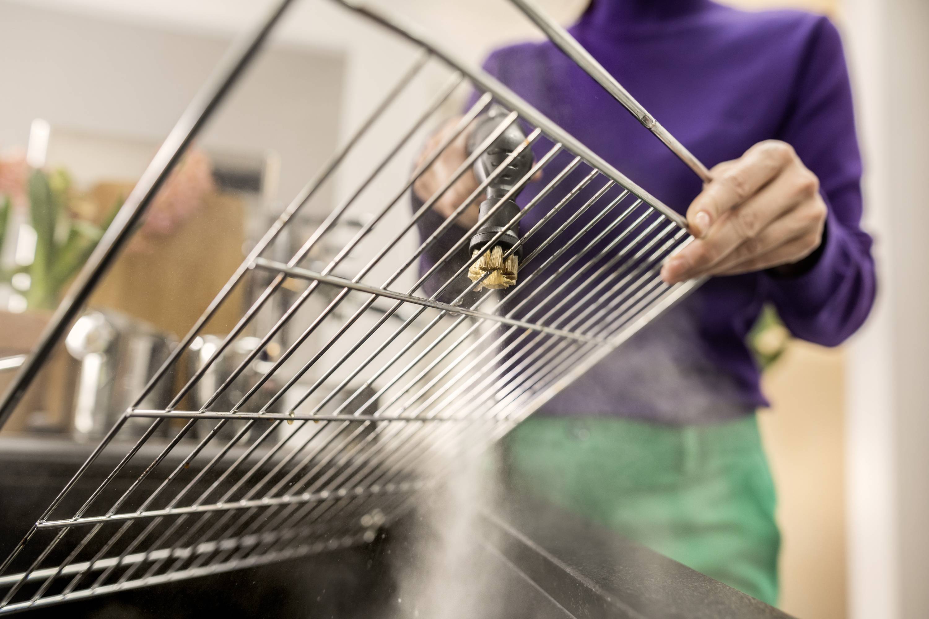 Une personne nettoie une grille métallique au-dessus d'un évier. De la vapeur s'élève pendant que la grille est rincée à l'eau.