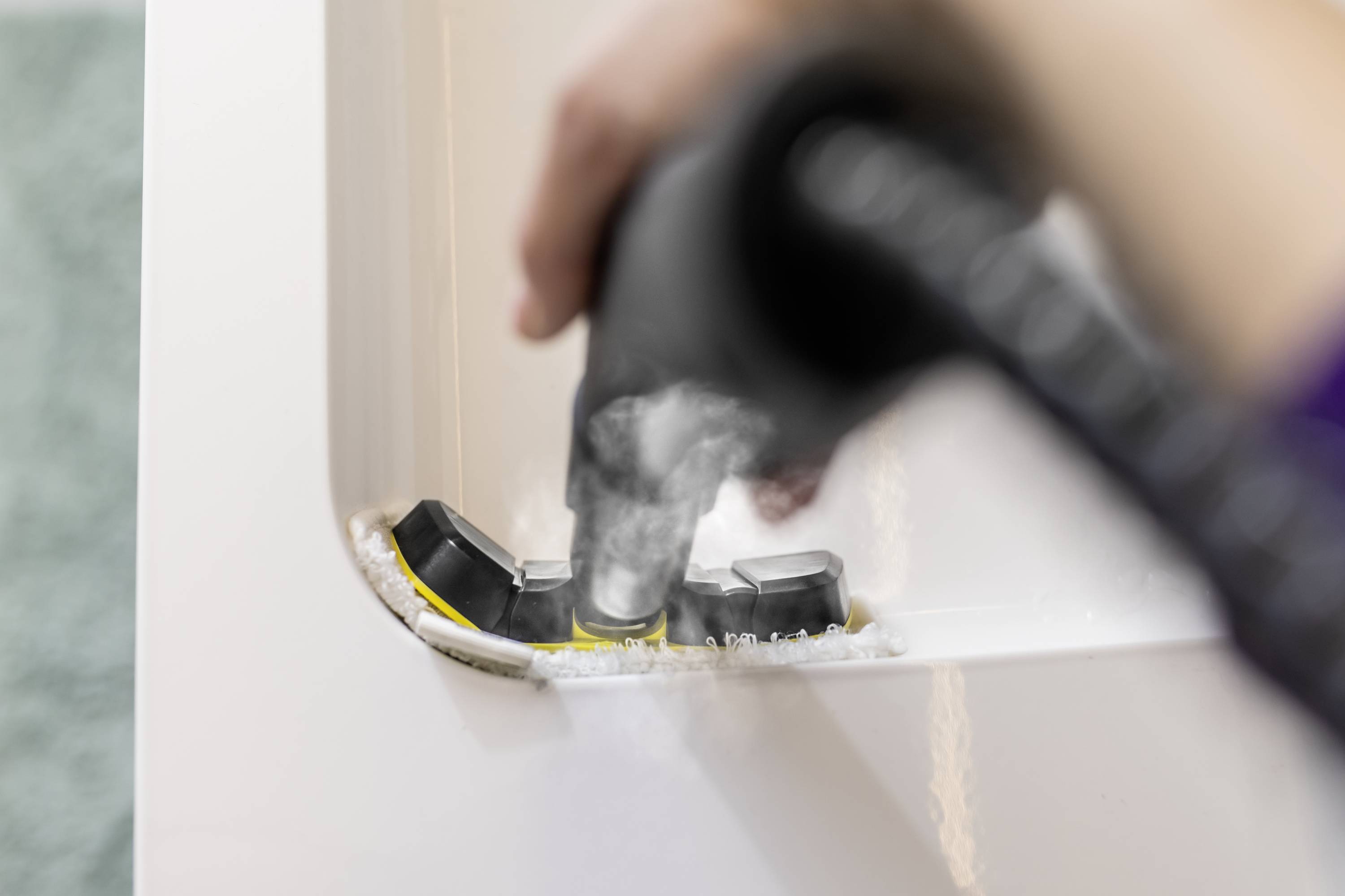 Une main nettoie une machine à café en vaporisant de l'eau sur les joints et les parties internes.