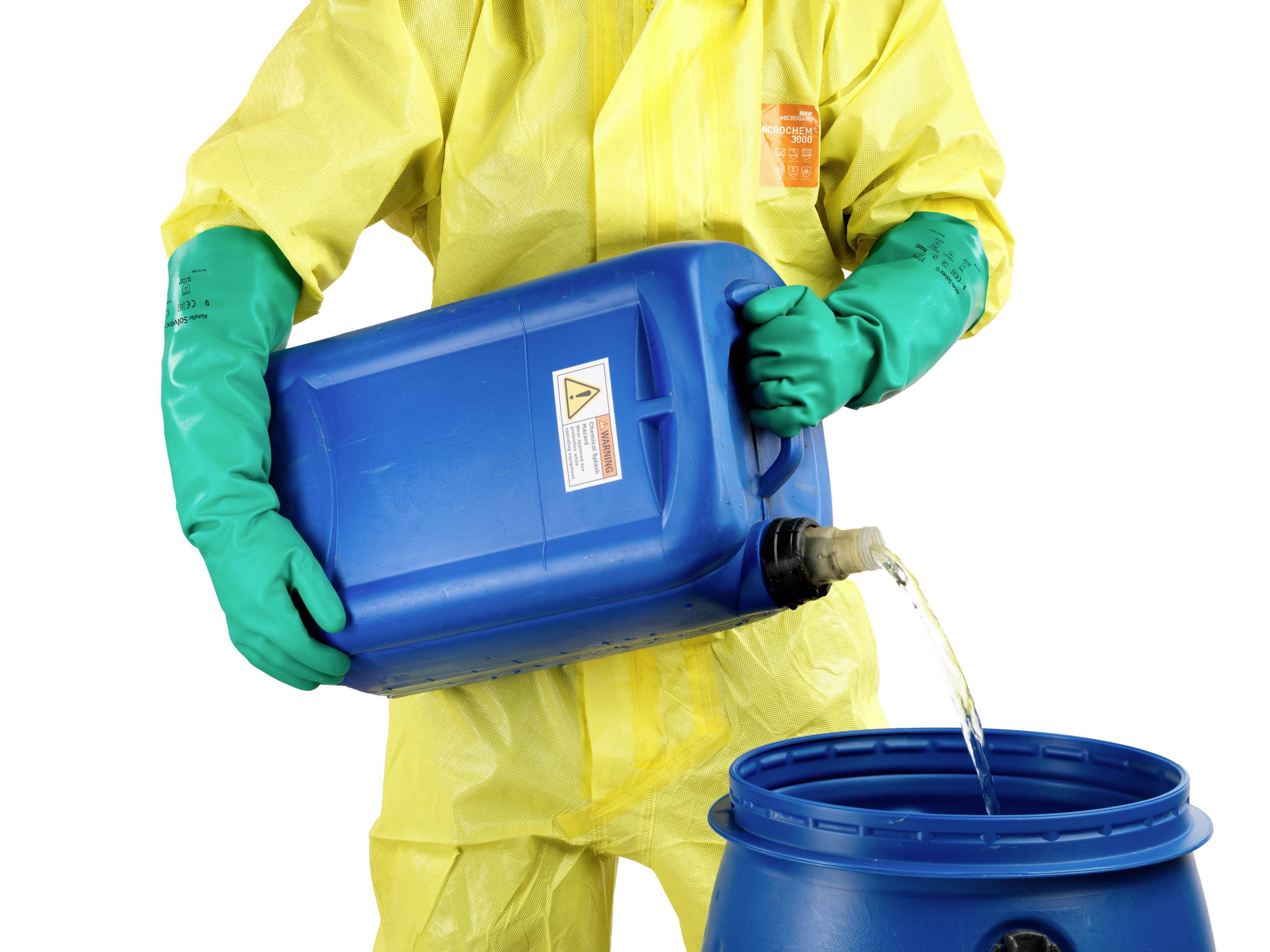 Une personne portant une combinaison de protection jaune et des gants verts verse un liquide d'un bidon bleu dans un tonneau bleu.