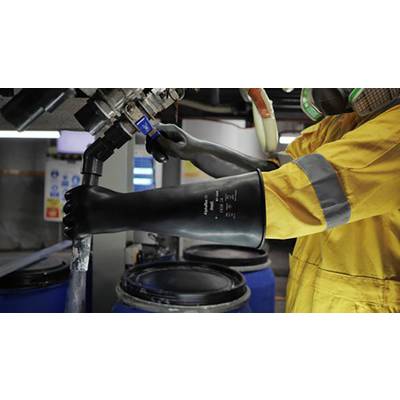 Une personne portant des vêtements de protection jaunes et des gants noirs actionne une vanne au-dessus de grands fûts bleus dans un environnement industriel.