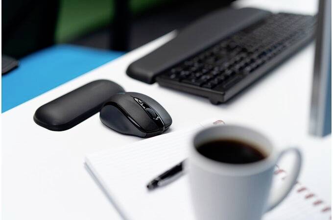 Une souris d'ordinateur et un clavier sont posés sur un bureau, à côté d'un bloc-notes ouvert et d'une tasse de café.