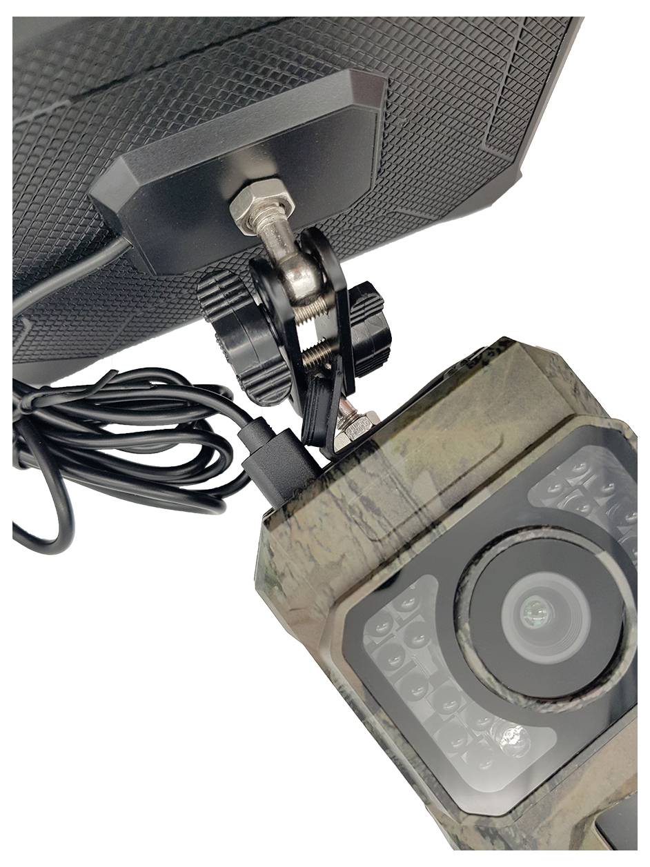 Caméra forestière en couleurs de camouflage, fixée sur un support noir, avec connexion câblée pour l'alimentation électrique.