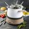 Un set à fondue électrique posé sur une table, entouré de légumes et de pain. De la vapeur s'élève du caquelon, quatre fourchettes à fondue y sont disposées.