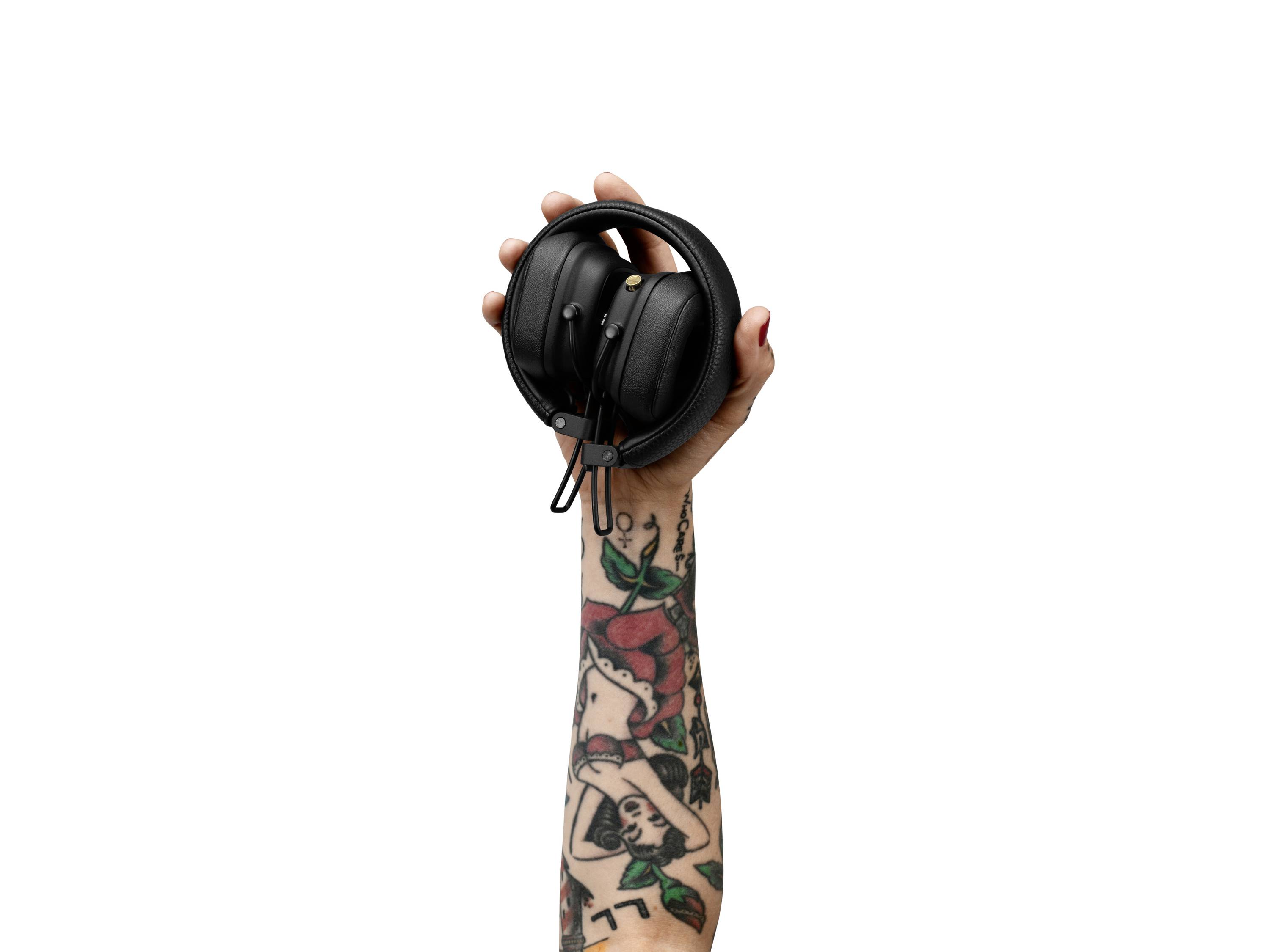 Une main tatouée tient une paire d'écouteurs noirs en l'air.