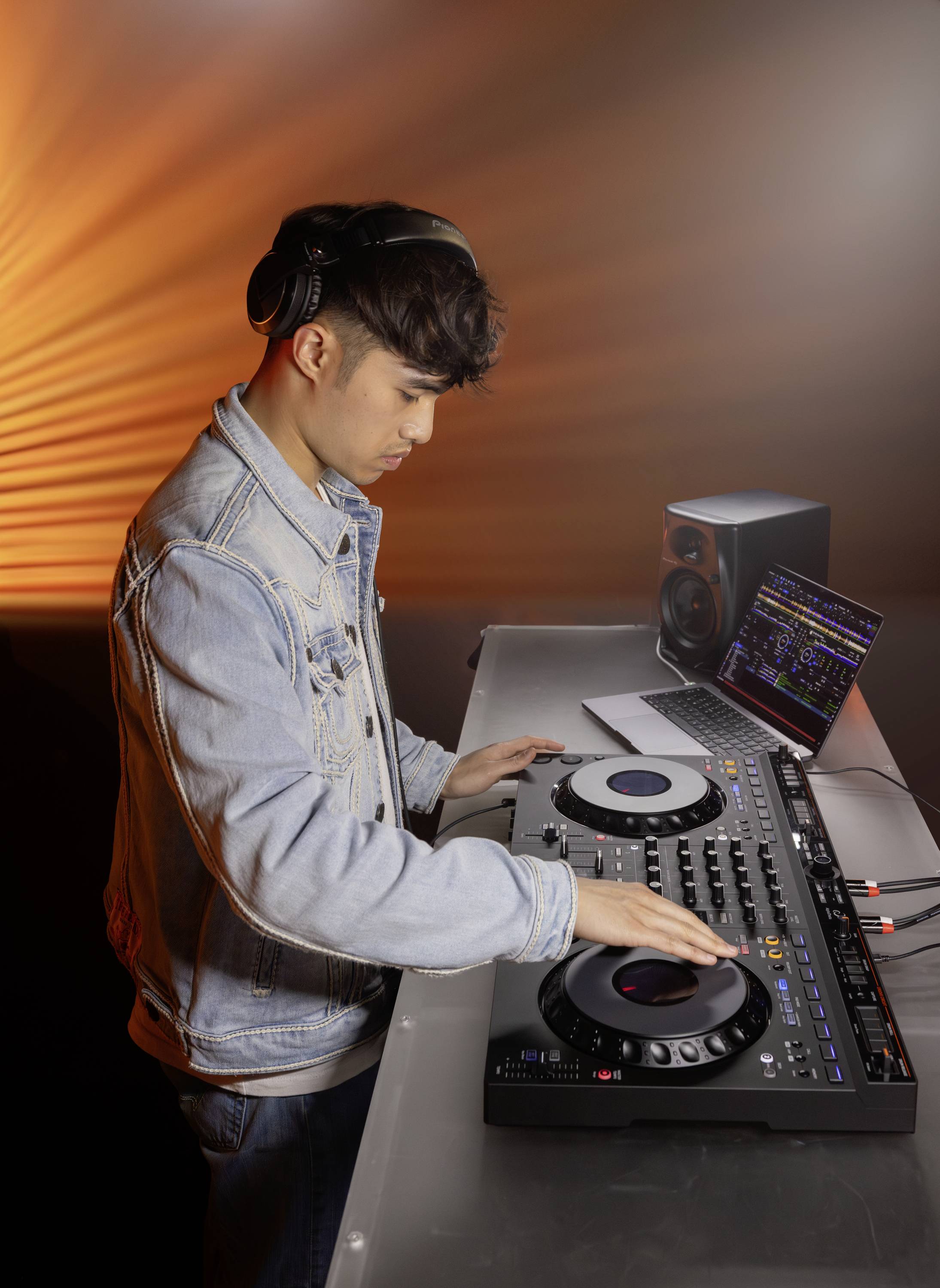 Une personne avec des écouteurs mixe de la musique sur une table de mixage. Des effets d'éclairage orange sont visibles en arrière-plan.