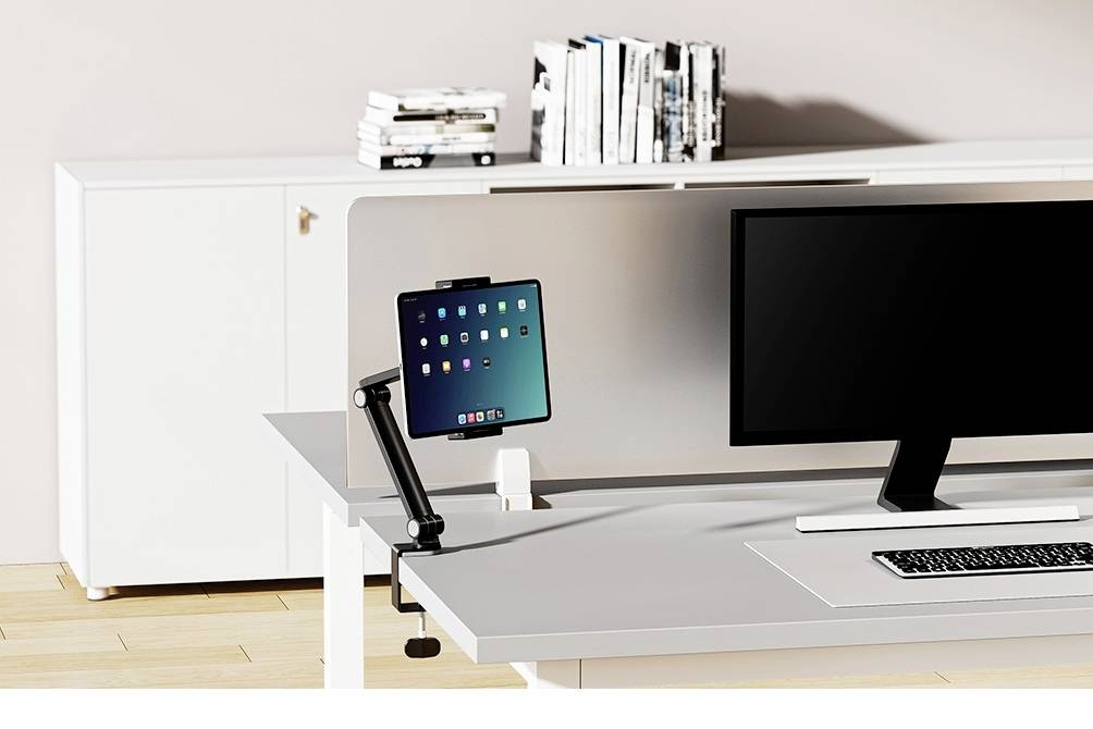 Un espace de travail moderne avec un grand écran, un clavier et une tablette sur un bras support, une bibliothèque en arrière-plan.