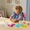 Un enfant aux cheveux bouclés est assis à une table et joue avec des jouets de construction colorés disposés devant lui dans différentes formes.