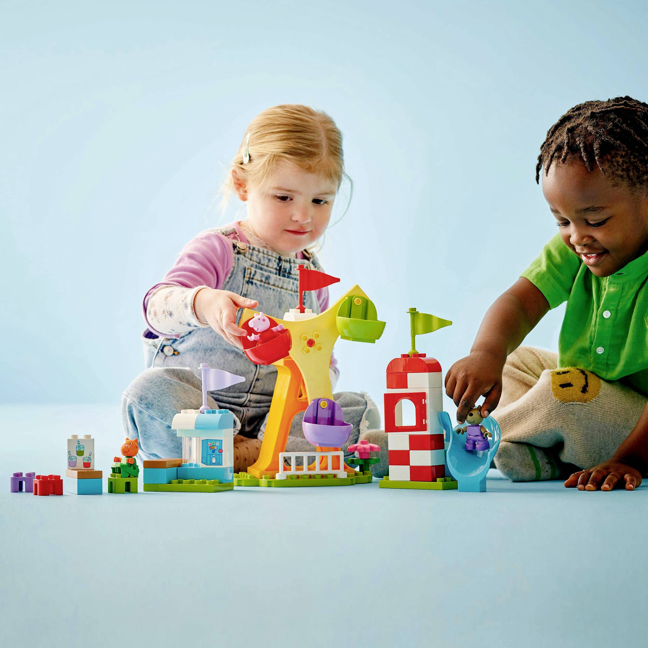Deux enfants jouent avec des blocs de construction colorés sur un fond bleu clair. Ils semblent concentrés et joyeux.