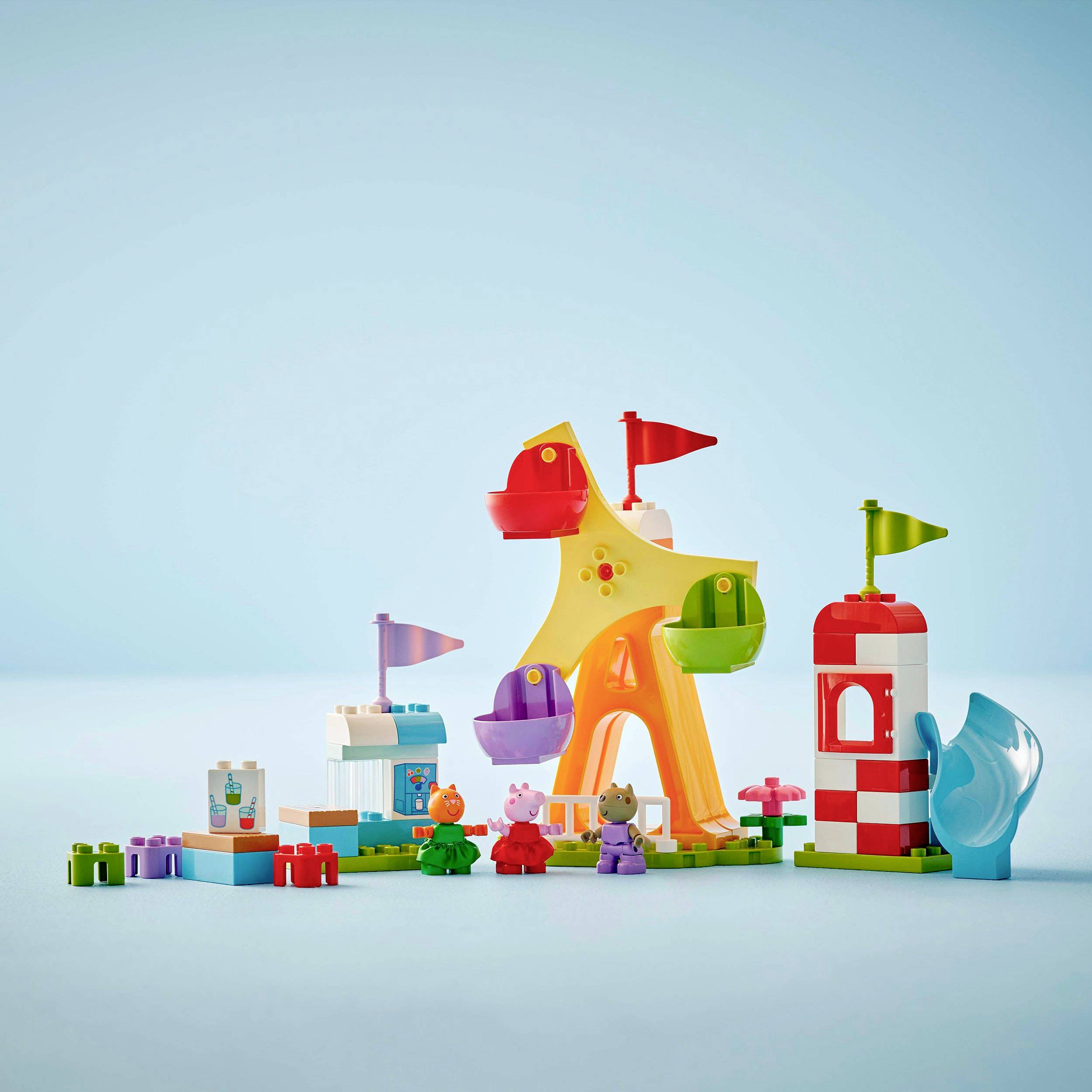 Paysage de jouets colorés composé de blocs de construction avec une tour, un carrousel et des figurines d'animaux sur un fond clair.