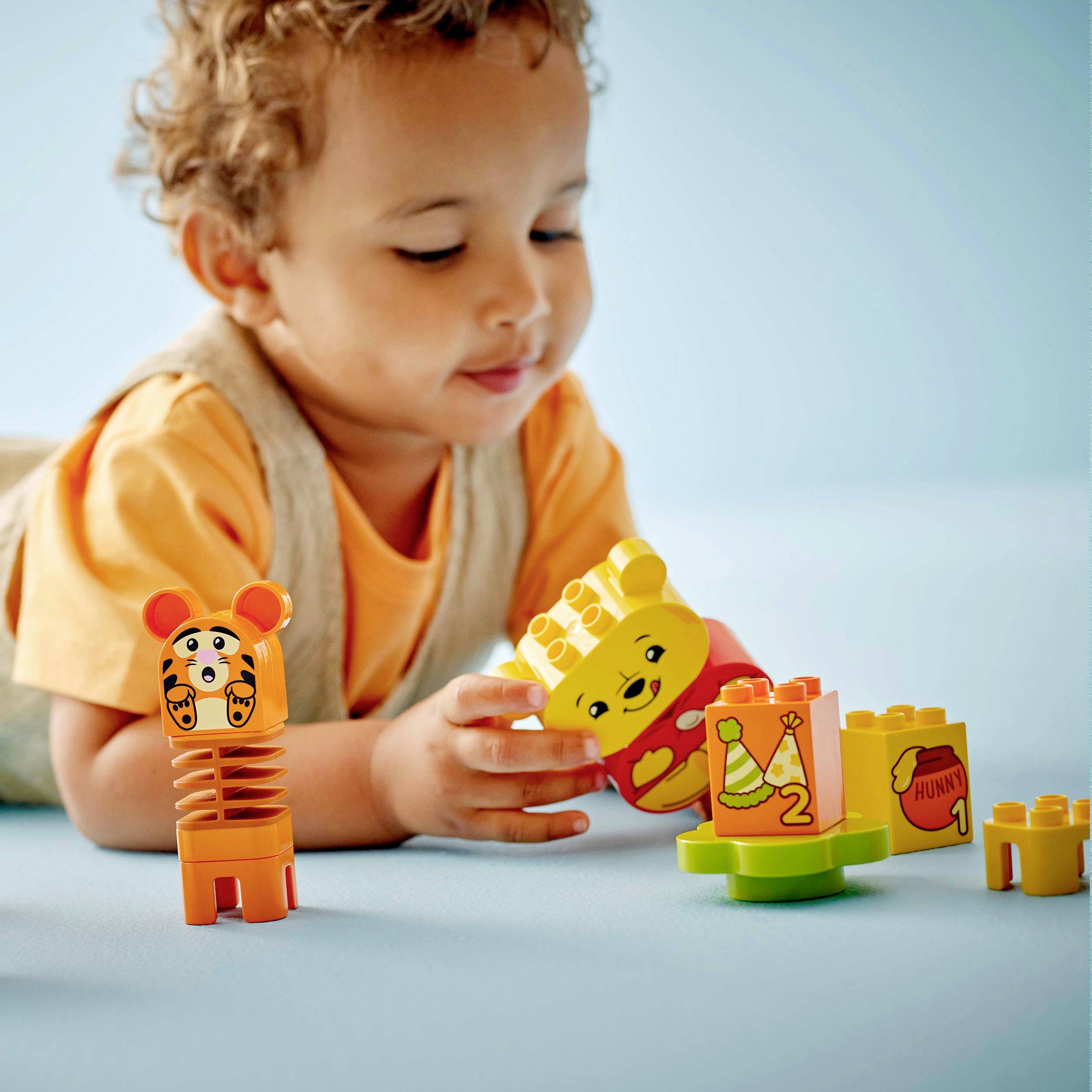 Un jeune enfant joue joyeusement avec des blocs colorés en forme d'animaux sur un sol bleu.