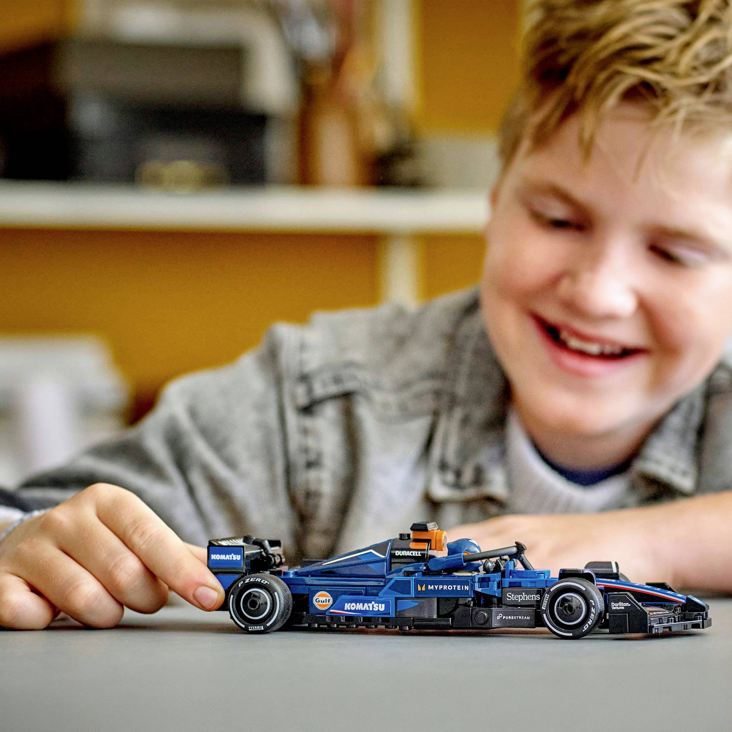 Un enfant joue avec un jouet de voiture de course bleu sur une table, un sourire aux lèvres. L'enfant est concentré et semble prendre beaucoup de plaisir.