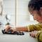 Un enfant joue avec concentration à une voiture de course miniature sur une table. Des objets flous en arrière-plan suggèrent un environnement domestique.