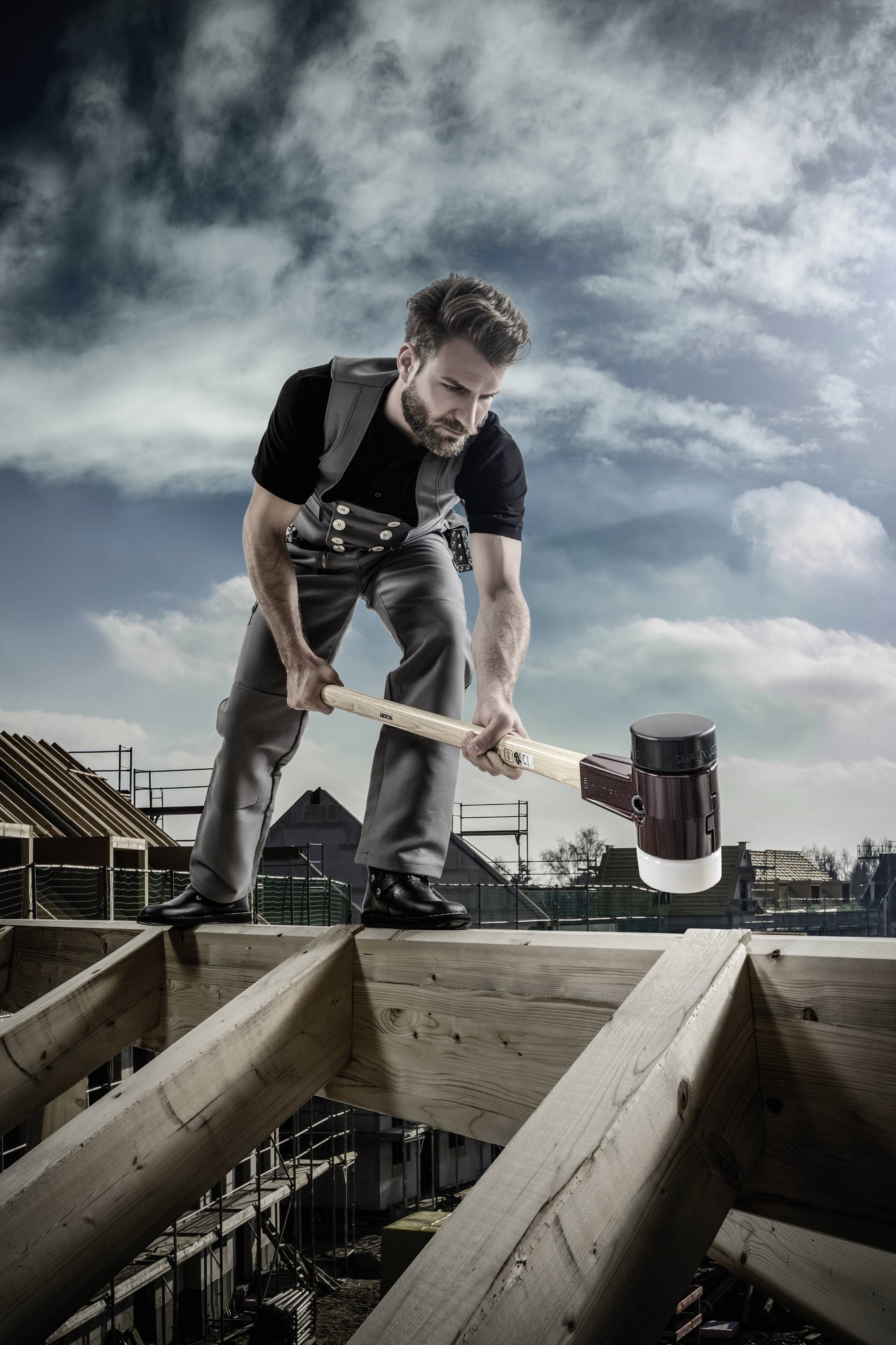 Un charpentier vêtu de vêtements de travail traditionnels travaille avec un grand marteau sur la charpente d'une maison en construction.