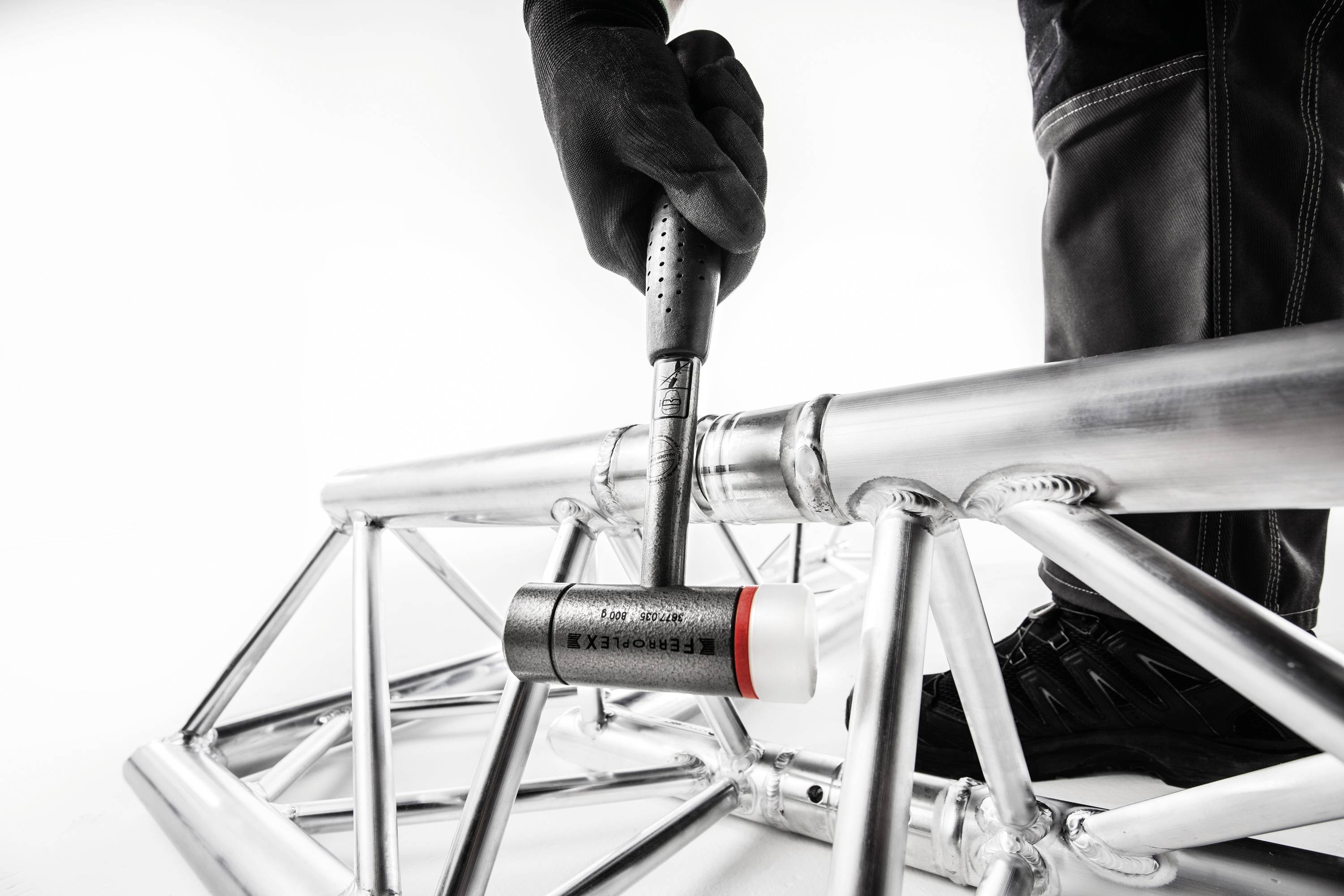 Une personne frappe un cadre en aluminium avec un marteau. La tête du marteau est marquée 'BERENTOOLS'.