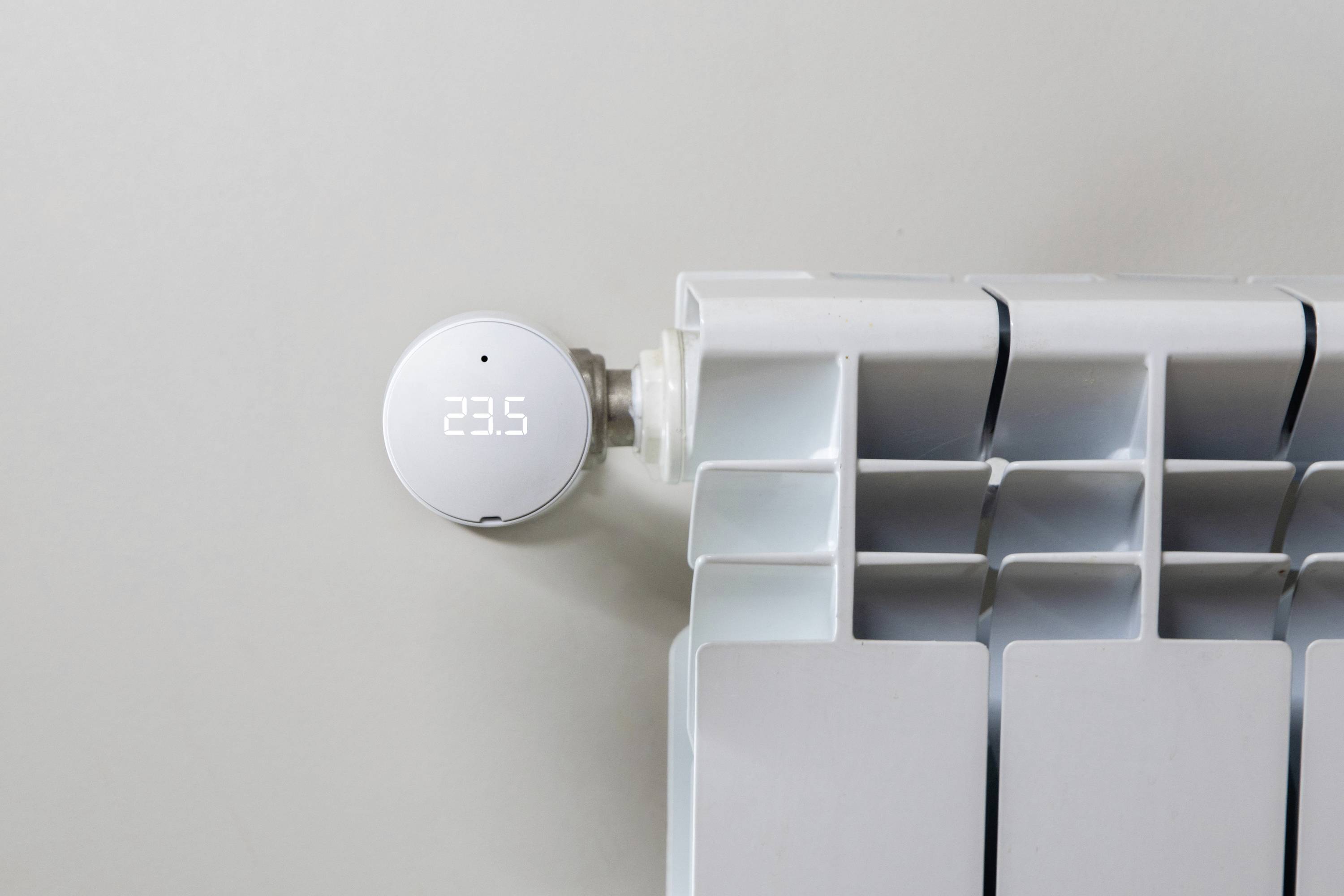 Un thermostat numérique affiche '23,5' et est fixé à un radiateur blanc.
