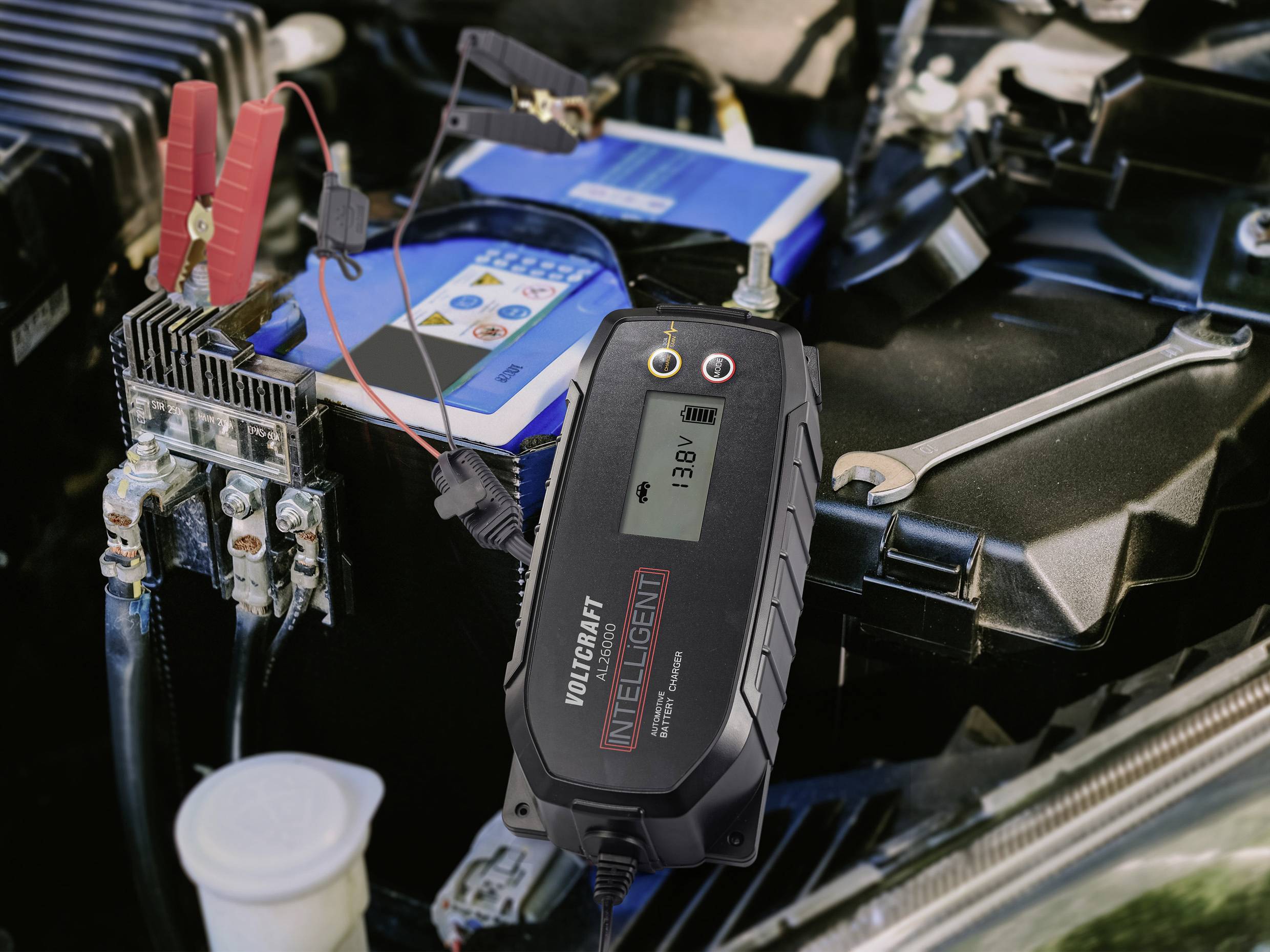 Un chargeur de batterie est connecté à une batterie de voiture. L'affichage indique '13,8V', ce qui signale le processus de charge.