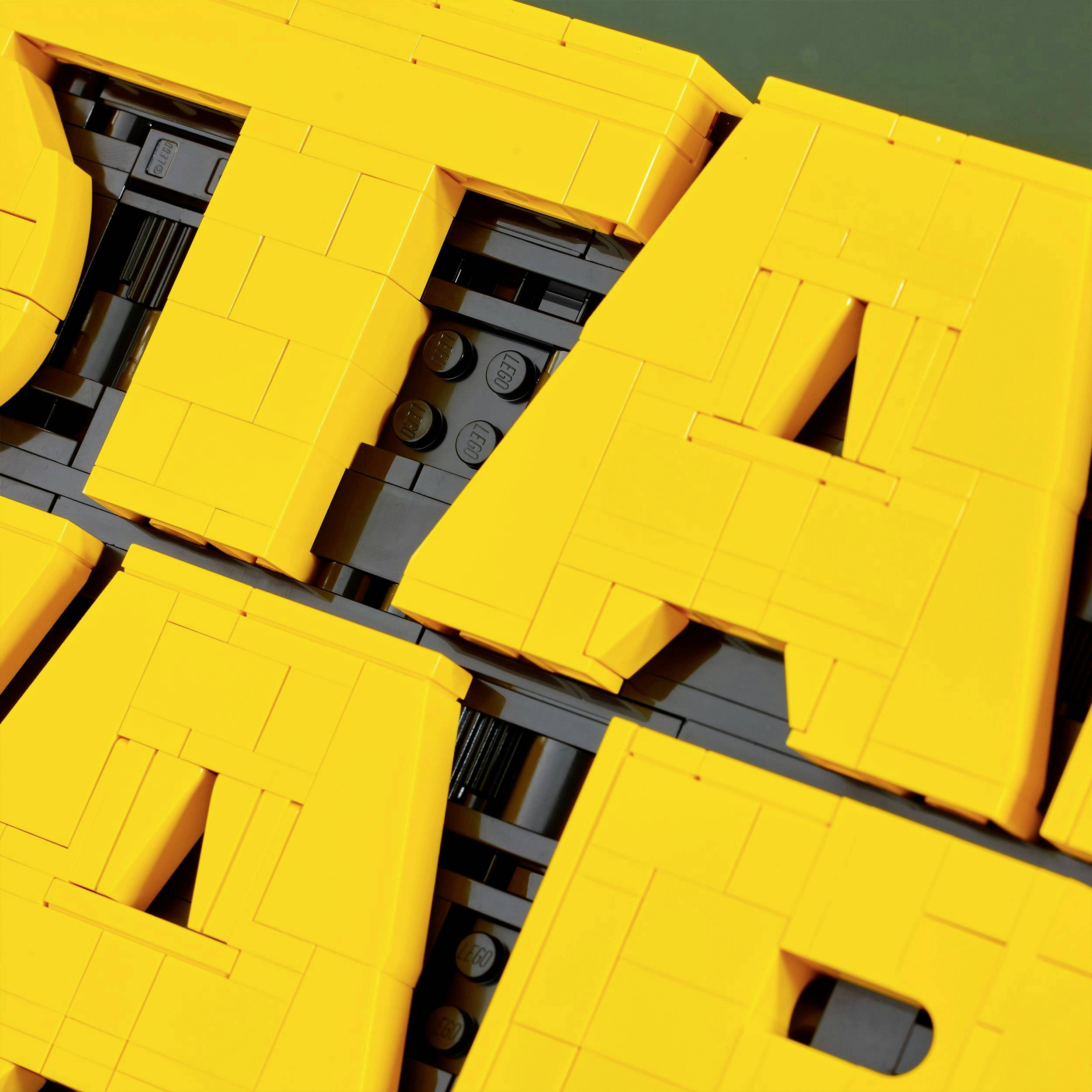 Des blocs LEGO jaunes forment de grandes lettres géométriques. Un gros plan révèle la structure et les détails des briques.