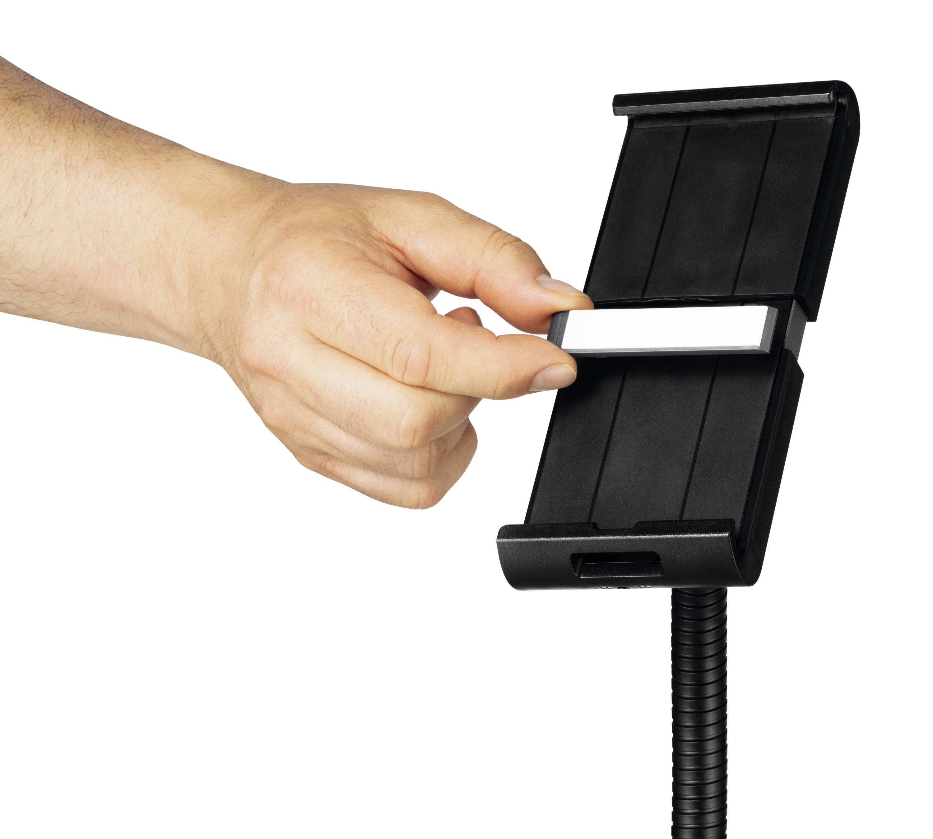 Une main tient un objet rectangulaire noir avec un support flexible.