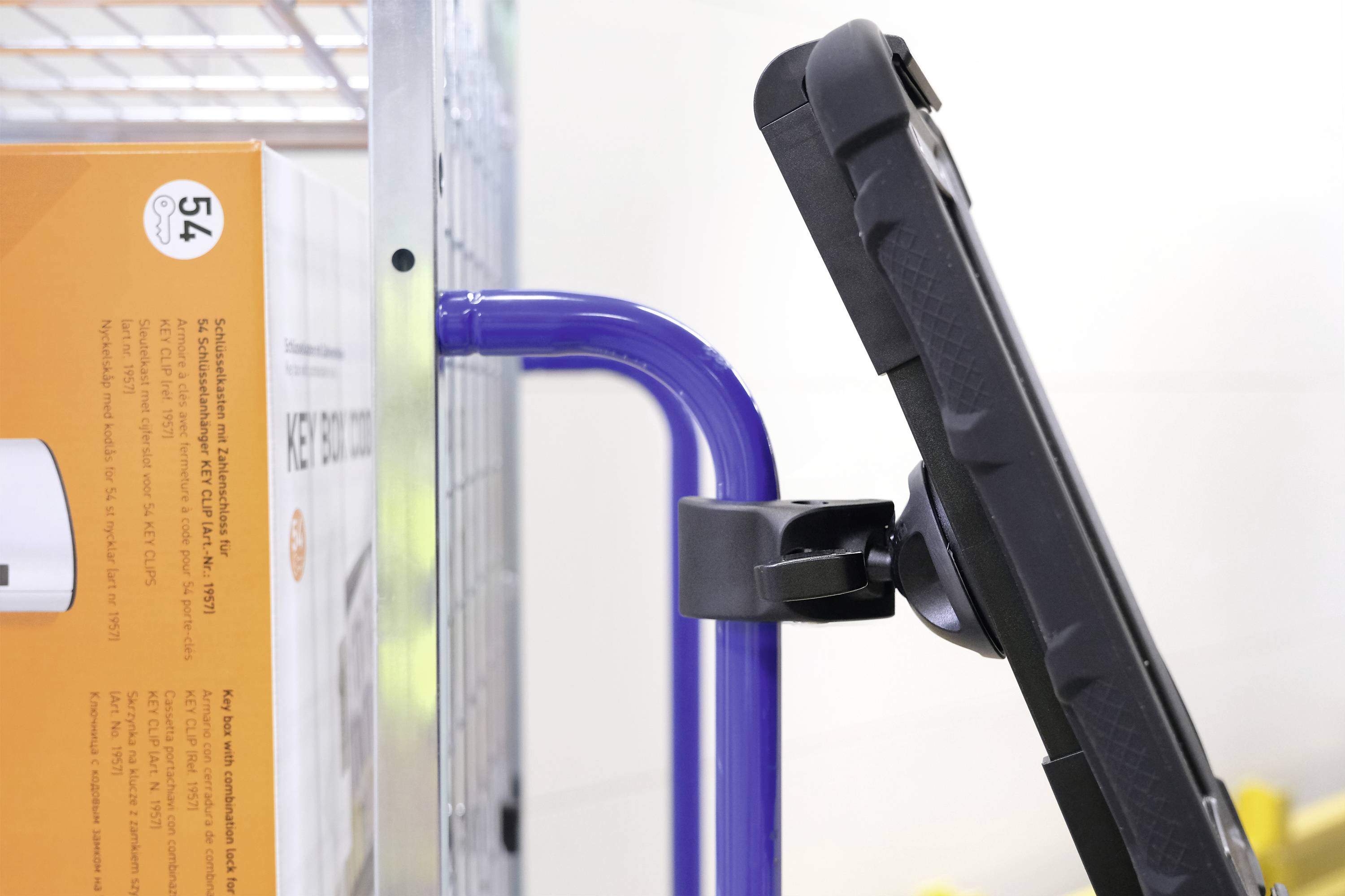 Une tablette est fixée à un chariot de supermarché. Un carton orange est visible sur le côté gauche.