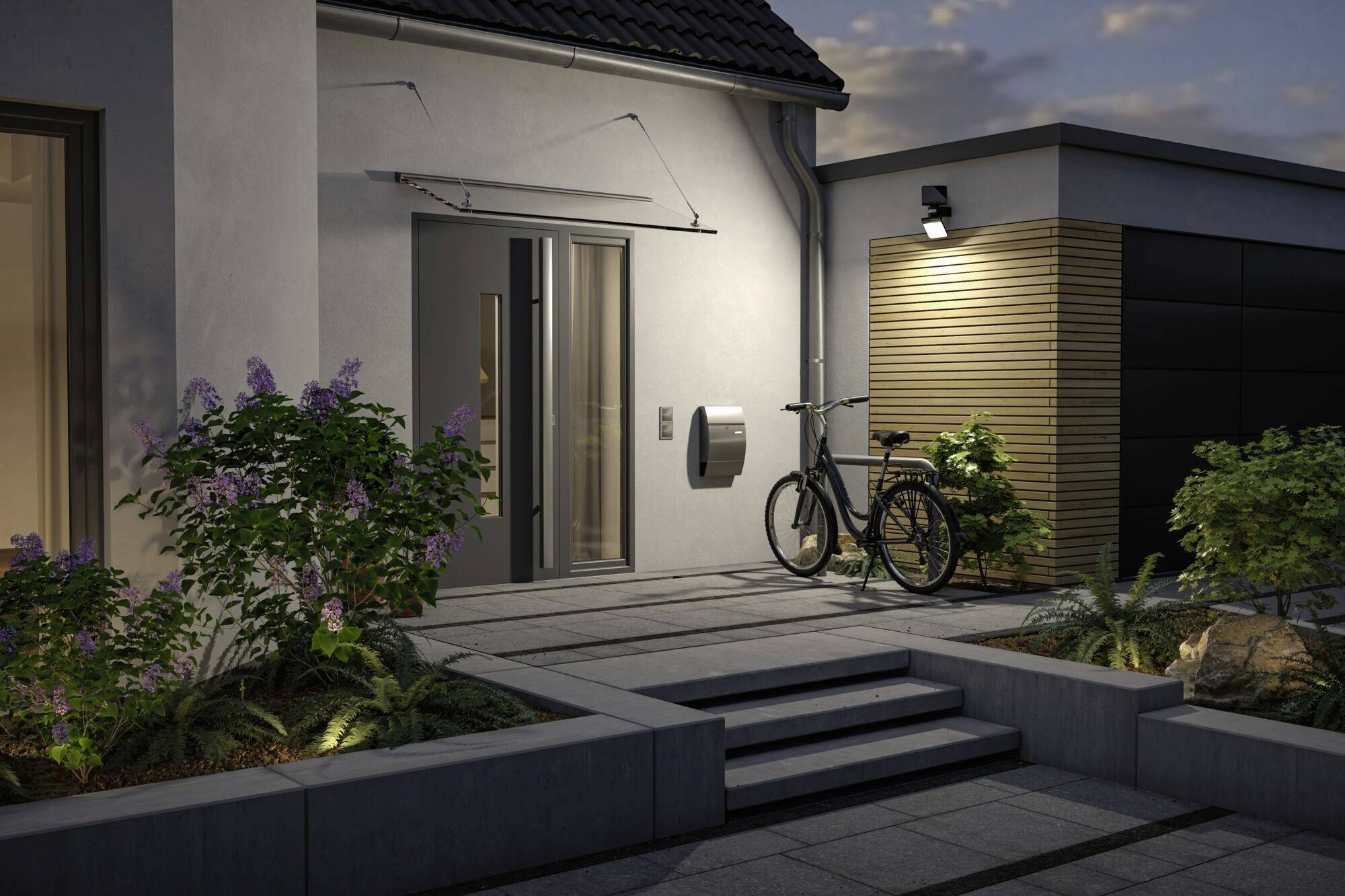 Maison résidentielle avec une porte d'entrée moderne, un vélo contre le mur, un éclairage et des plantes dans le jardin avant. L'ambiance du soir renforce l'atmosphère chaleureuse.