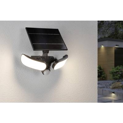Lampe solaire avec deux spots et détecteur de mouvement fixée sur un mur de maison, illuminant une zone d'un jardin moderne.