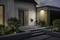 Une maison moderne avec un jardin avant au crépuscule. Un vélo est stationné à côté de la porte d'entrée, éclairé par une lumière extérieure chaleureuse.