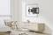 Salon au design moderne, avec un fauteuil blanc et un buffet. Un support mural est installé pour la télévision. Pièce lumineuse avec un sol en bois.