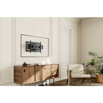 Support mural sans téléviseur installé sur un mur peint, à côté une table en bois avec décoration, un fauteuil et une plante.