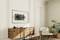 Support mural sans téléviseur installé sur un mur peint, à côté une table en bois avec décoration, un fauteuil et une plante.