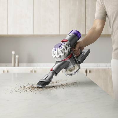 Une personne utilise un aspirateur sans fil pour enlever des miettes d'un plan de travail de cuisine.