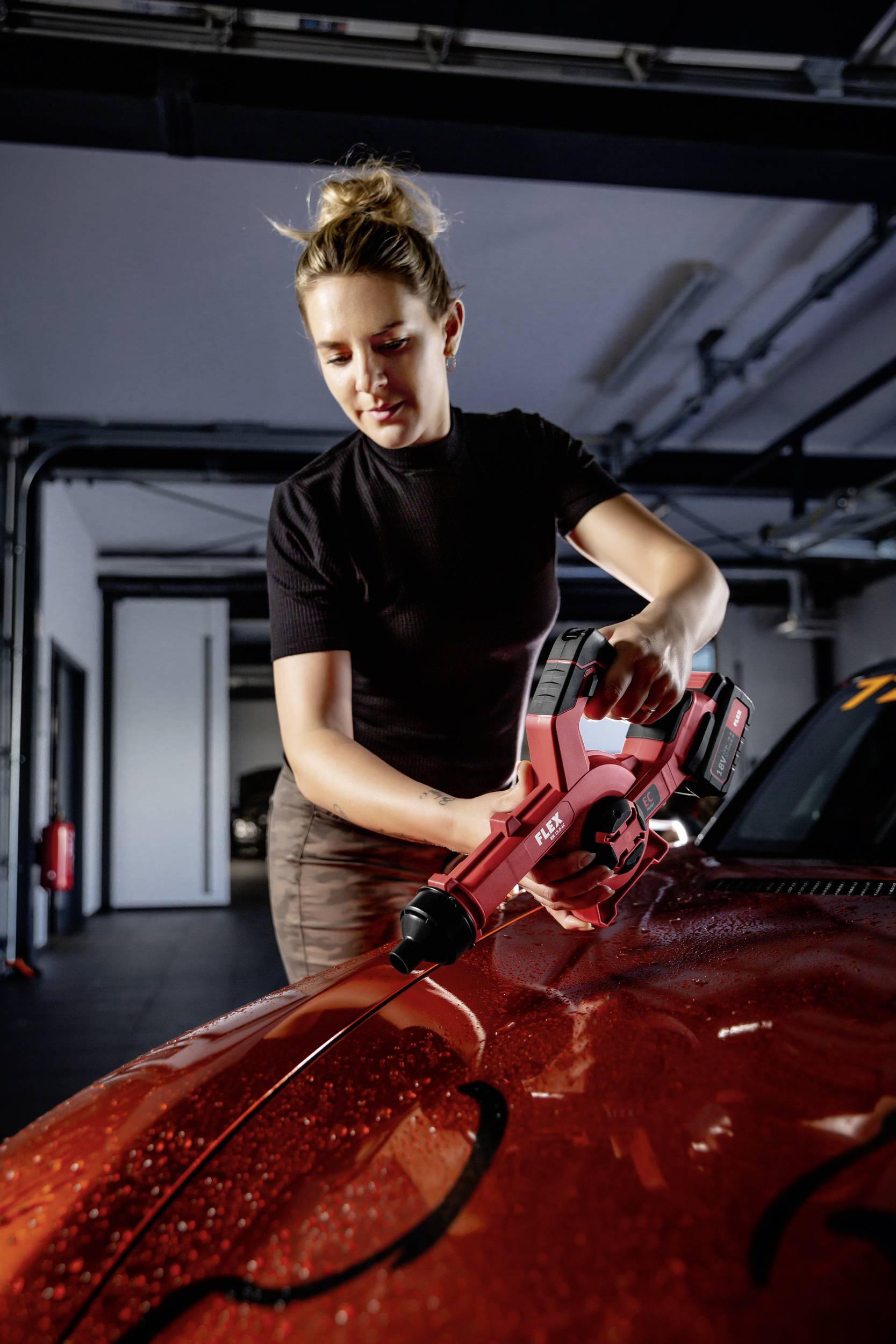 Une personne polit le capot d'une voiture rouge à l'aide d'une polisseuse rouge dans un garage.