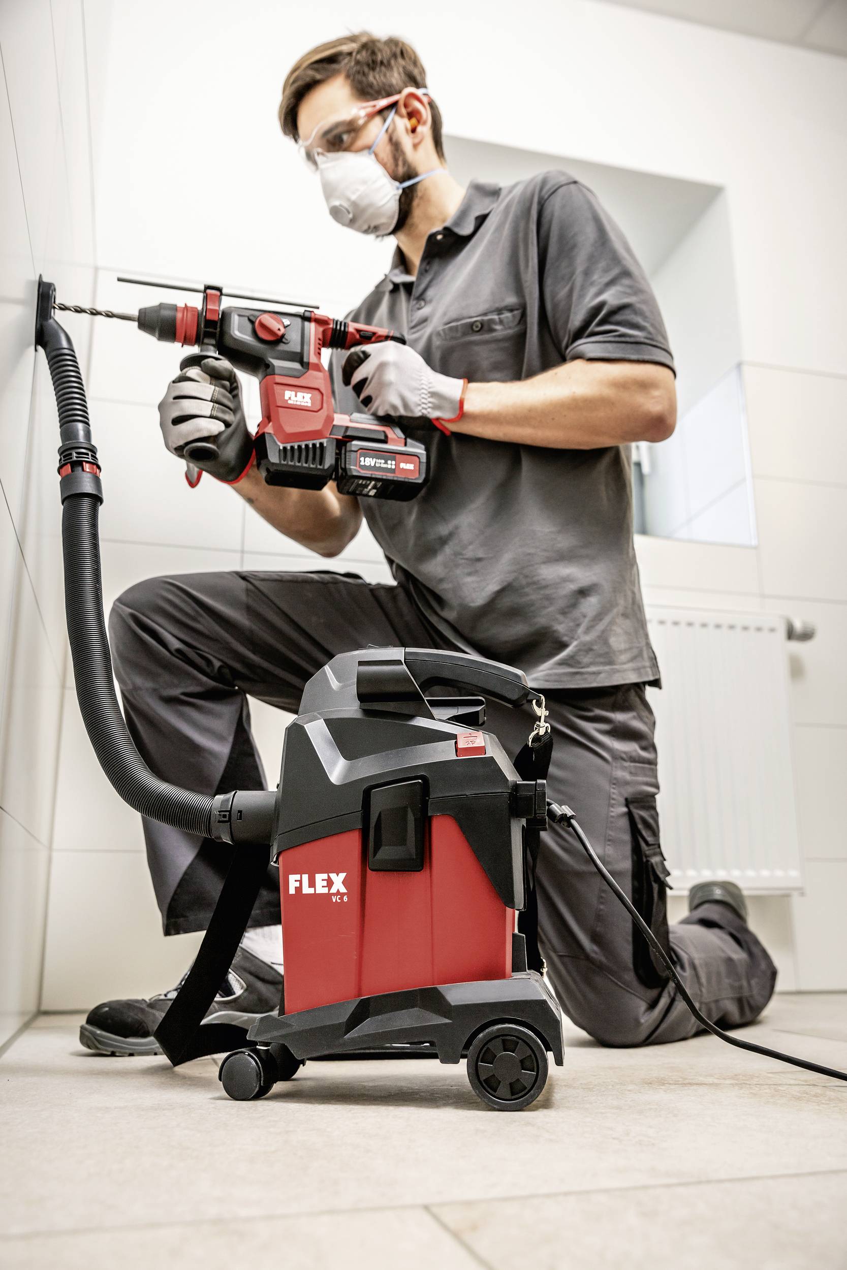 Un homme fore un mur avec une perceuse puissante, accompagné d'un aspirateur qui aspire la poussière en train de se former.