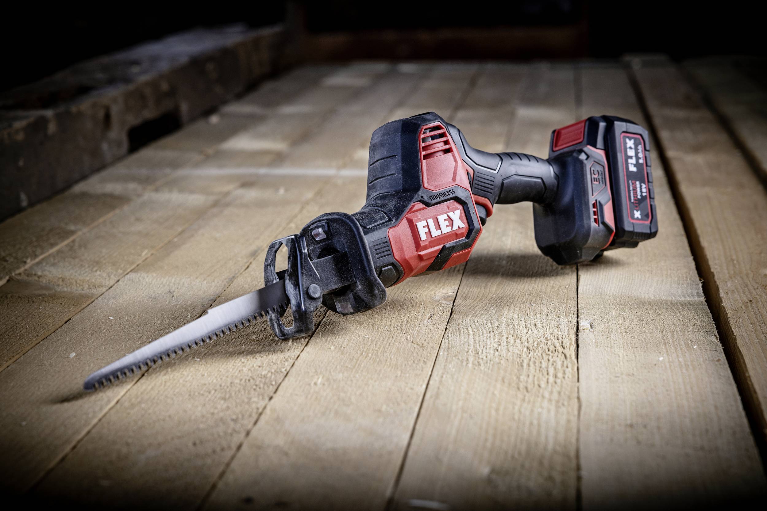 Une scie sabre sans fil repose sur des planches de bois. Elle est noir et rouge et affiche le nom de la marque. L'environnement ressemble à un chantier de construction.
