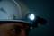 Une personne porte un casque de protection équipé d'un projecteur frontal dans une pièce sombre, ce qui suggère un travail dans un environnement obscur.