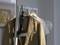 Un costume beige est suspendu à un cintre, à côté d'une chemise blanche. Un fer à repasser à vapeur est fixé à la tringle.