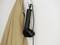 Un fer à repasser vapeur noir est suspendu à un crochet sur le mur. À côté, un manteau beige est accroché.