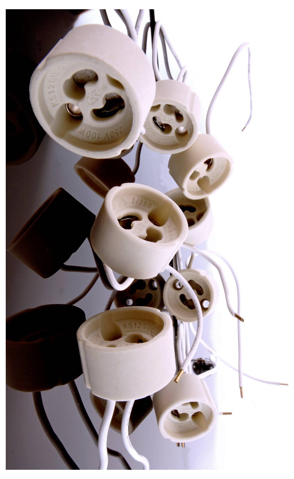 Gros plan de plusieurs douilles de lampe électriques suspendues, avec des fils et cordons dénudés, sur fond blanc.