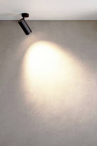 Un mur est éclairé par un projecteur de plafond qui projette une lumière focalisée sur une surface neutre.