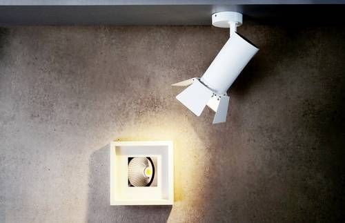 Un projecteur blanc illumine une petite œuvre d'art carrée sur un mur en béton.