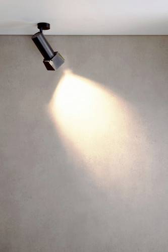 Un projecteur de plafond unique illumine un mur nu de manière ponctuelle, créant une sensation de minimalisme et de concentration.