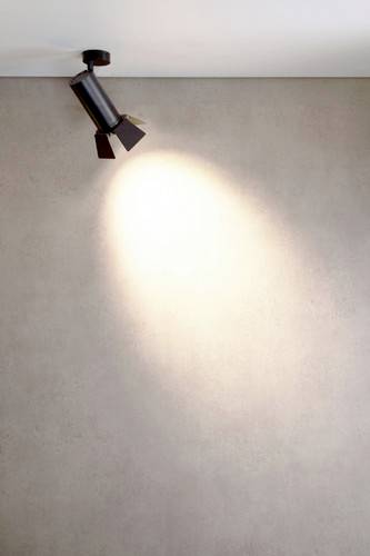 Un projecteur de plafond unique éclaire un mur et crée un cône de lumière sur la surface au coloris neutre.