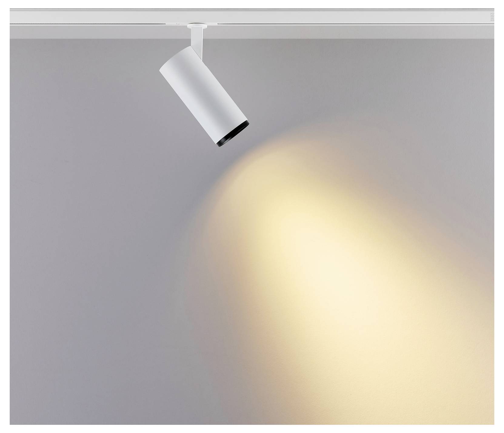 Spot de plafond blanc orienté vers le bas, projetant un faisceau chaleureux sur un mur gris.