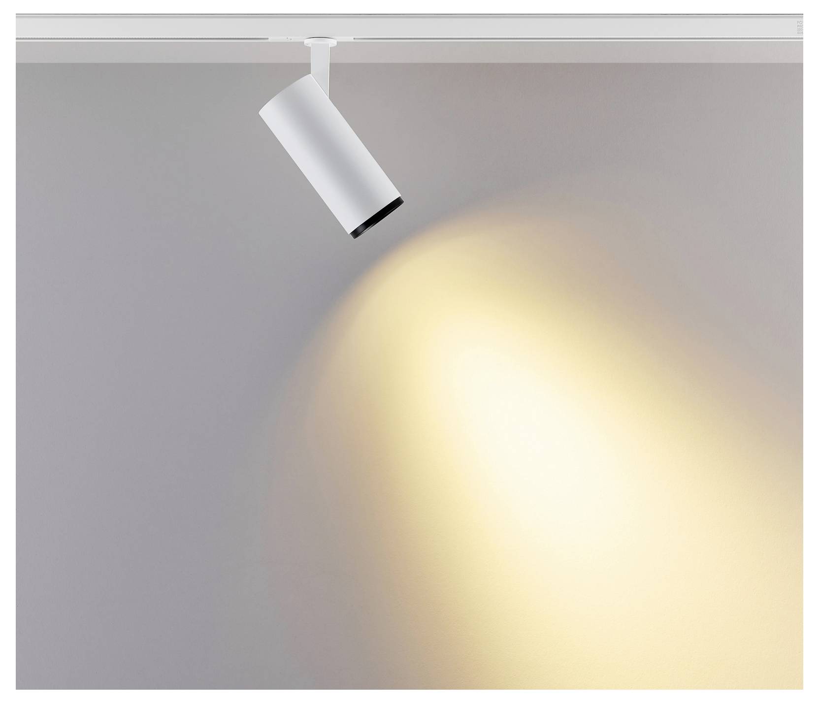 Spot de plafond blanc orienté vers le bas, projetant un faisceau circulaire chaleureux sur un mur gris.