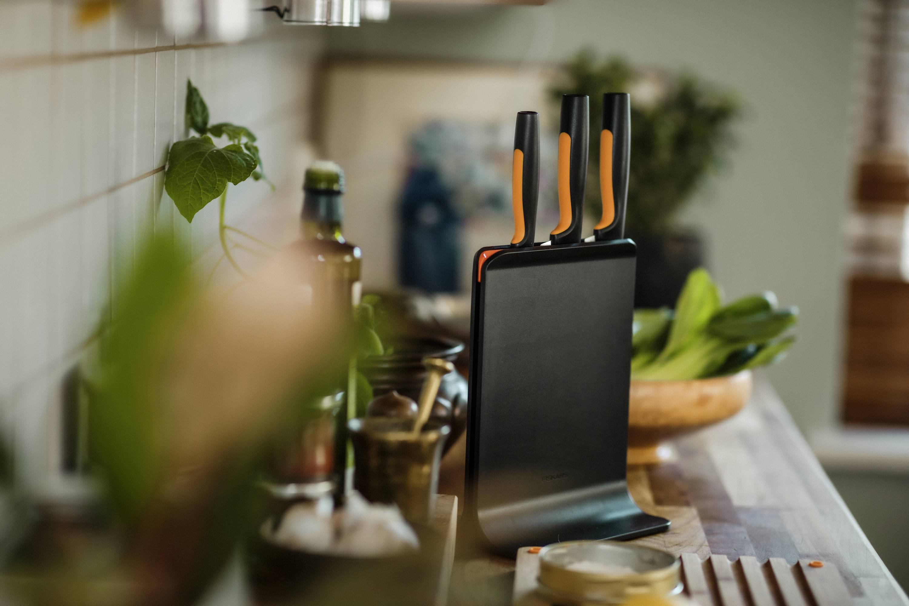 Bloc de couteaux noir avec trois couteaux dans une cuisine moderne, entouré d'ustensiles de cuisine et d'herbes.