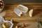 Du fromage râpé sur une planche en bois à côté d'un morceau de fromage à pâte dure et d'oignons. Une râpe blanche et orange est posée à proximité.