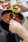 Une personne verse de l'huile d'olive dans une poêle contenant de la sauce tomate, avec un plan de travail de cuisine en arrière-plan.